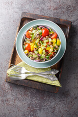 Fresh salad with cherry tomatoes, celery, yellow pepper, black-eyed peas, cucumber and onion close-up in a bowl on the table. Vertical top view from above