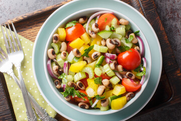 Summer salad with cherry tomatoes, celery, yellow pepper, black-eyed peas, cucumber and onion close-up in a bowl on a wooden board. horizontal top view from above