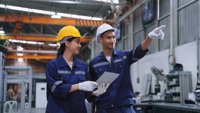 Smart engineer worker man and woman in uniform safety and wear helmet consulting and using tablet help analyze data in warehouse at manufactory. Industrial and factory warehouse concept