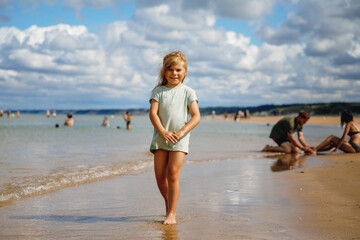 Happy preschool girl having fun on the sand beach Omaha at Atlantic coast of Normandy, France. Outdoor summer activities for kids
