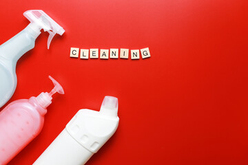 Flat lay cleaning products, cleaning spray on red background and sponges. Word cleaning from wooden letters