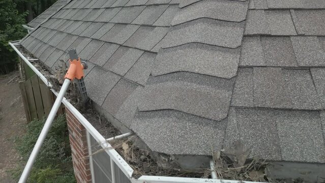 Cleaning out dirty, blocked gutters from the ground, with a plastic scoop on a pole.