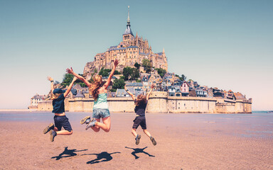Happy family jumping in front of Mont Saint Michel-  vacation, travel destination, tour tourism concept - obrazy, fototapety, plakaty