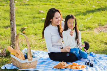 Happy Asian mother and little girl daughter child having fun and enjoying outdoor together sitting...