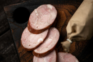 Stick of sausage is cut into pieces. Smoked sausage in paper wrapper on wooden board. Wooden dark...