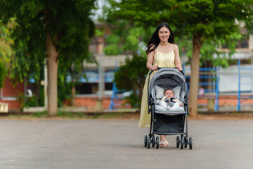 happy mother pushing infant baby stroller and walking in park