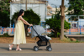 mother pushing infant baby stroller and walking in park
