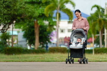 happy mother pushing infant baby stroller and walking in park