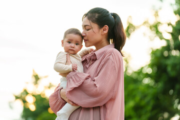 mother holding and kissing her infant baby in park with sunlight