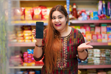 Indian woman showing smartphone screen at grocery shop.