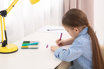 Cute little girl drawing with marker at desk in room. Home workplace