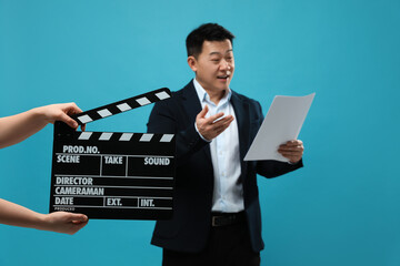 Happy asian actor performing role while second assistant camera holding clapperboard on light blue...