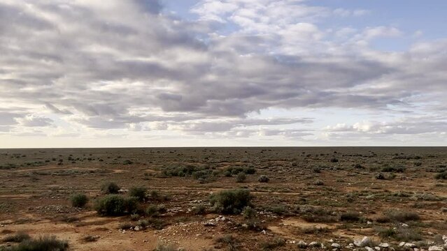 Indian Pacific Train travels through the vast, barren Western Australian Nullabor Plain on cloudy day. Low scrub & saltbush survives in red dirt