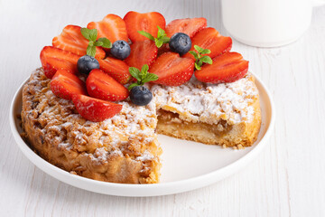 Sweet cake with strawberries on plate on white wooden background