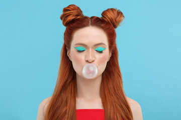 Naklejka premium Beautiful woman with bright makeup and closed eyes blowing bubble gum on light blue background