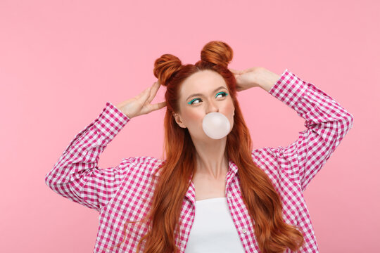 Beautiful woman with bright makeup blowing bubble gum on pink background