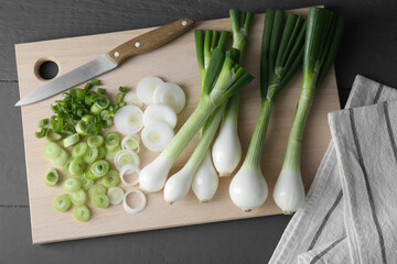 Board with knife, whole and cut spring onions on grey wooden table, flat lay