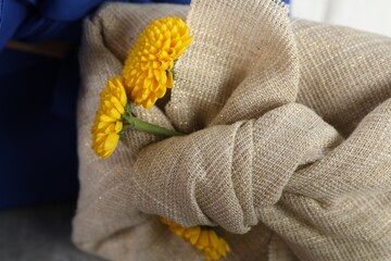 Fototapeta na wymiar Furoshiki technique. Gift packed in beige fabric with yellow chrysanthemum flowers, closeup