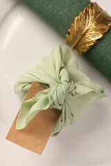 Furoshiki technique. Gift packed in green fabric, blank card and napkin on plate, top view
