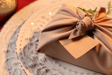 Furoshiki technique. Gift packed in beige fabric, with blank card on plate, closeup