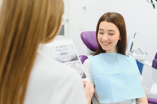 The dentist shows the x-ray image to the patient. People, medicine, dentistry, technology and healthcare concept. Woman dentist with x-ray image of teeth and female patient in dental clinic office.