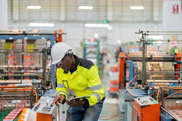 African male engineer technician manager Man pushing Swiss button, electronic machine, holding tablet, wearing safety helmet and vest in plastic and steel manufacturing factory.