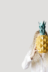 Summer conceptual photo woman hide head in paper pineapple. Girl with long hair hold tropical fruit. Summertime party, celebration, vacation concept, positive mood. Minimal style, trend photo