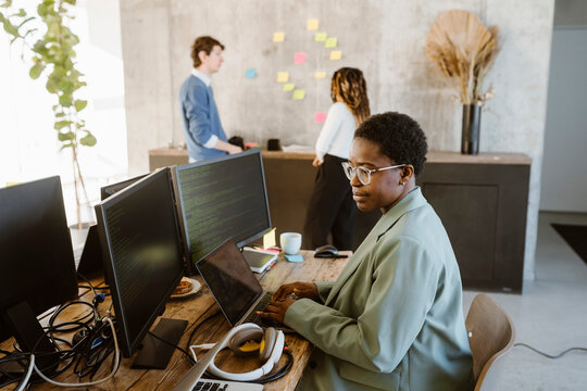 Side view of female programmer working on computer at desk in creative office