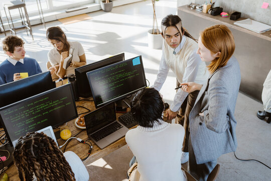 Businesswoman discussing with male and female programmers at desk in startup office