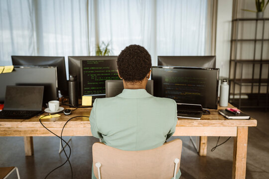 Rear view of female programmer working on computer in creative office