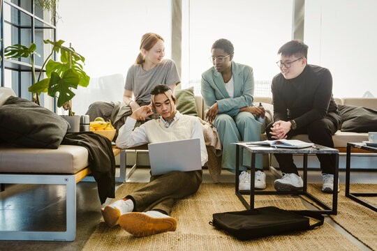 Multiracial male and female colleagues discussing over laptop in creative office