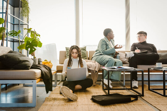 Programmer using mobile phone sitting on carpet while colleague discussing in creative office