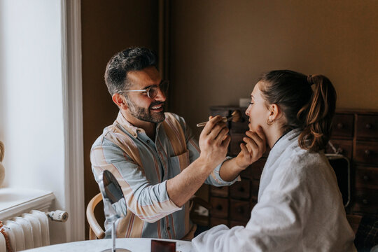 Smiling boyfriend applying make-up to non-binary person at home