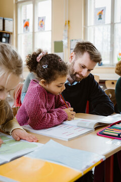 Schoolgirl solving maths equation by male teacher in classroom