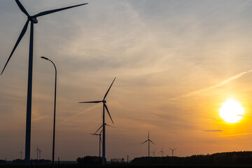 Wind turbines against the background of an orange setting sun. Renewable energy sources in the fight against high energy costs