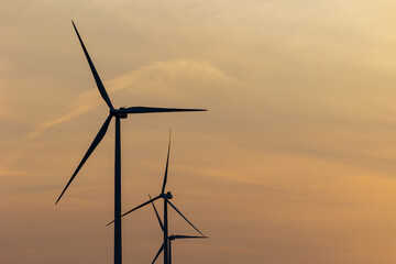 Fototapeta premium Wind turbines against the background of an orange setting sun. Renewable energy sources in the fight against high energy costs