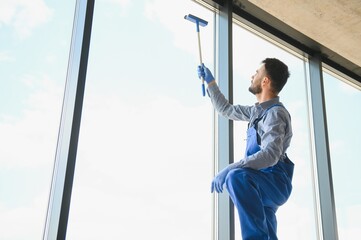 Male janitor cleaning window in office