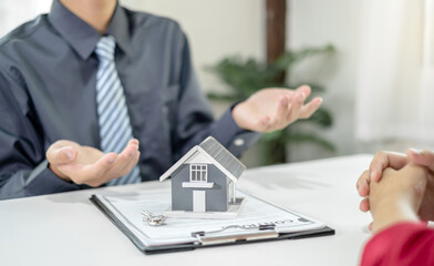 A real estate agent with a home model is talking to clients about renting a house and buying home insurance and contracting the contract after the formal negotiation is completed