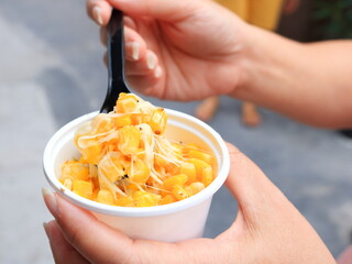 Corn and melt cheese stretches in white cup with hand hold black plastic spoon.