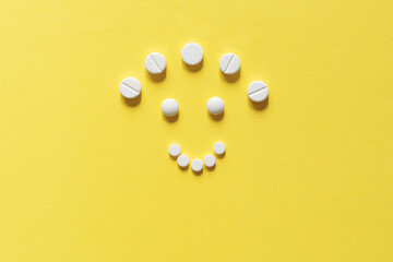 White round pills on a yellow background. Vitamin D, sun. Happy cheerful man smiley. Vitamins of happiness. Copy space, top view, mockup.	