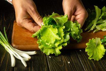 A man prepares lettuce and onion salad on the kitchen table. Healthy vegetarian food by the hands of the cook at home