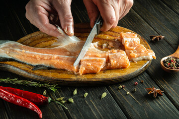 Male hands with a knife clean red fresh fish on a wooden cutting board. Home cooking of a delicious fish dish according to an old recipe