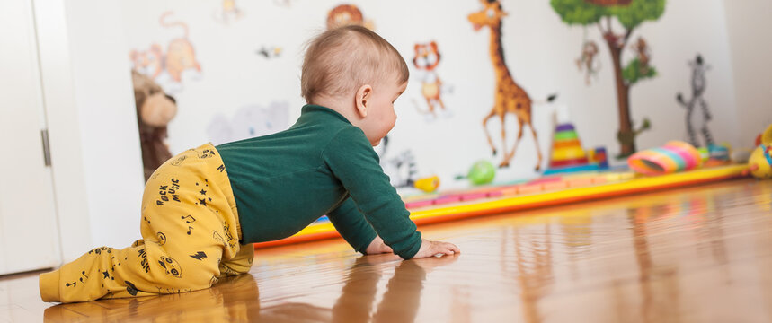 Cute baby boy crawls on the home floor, explore the world and learn to move. Side view. Love and family emotion