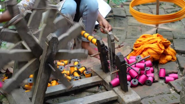 Woman spinning cotton thread by hand outside her house. The yarn is twisted into a reel through a process to make cloth. 