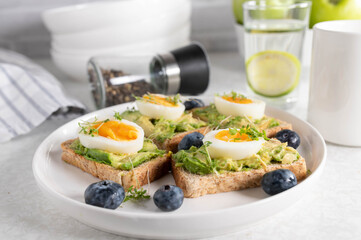 Breakfast toast with avocado spread, boiled eggs and cress on a plate. Served with a glass of water...