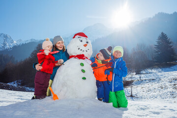 Family with mother and three children play building snowman