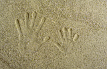 Handprints of an adult and a child in the sand. Summer mood.