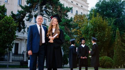 Excited amazing looking graduate lady posing with diploma together with her dad in front of the camera very excited smiling