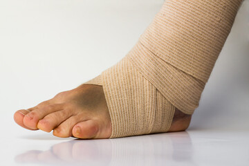Medical bandage correctly wrapped around female sprained left ankle stand on white background with the reflection and copy space