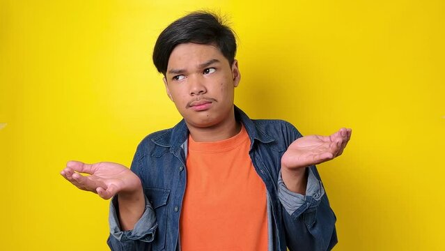 Don't know answer. Confused clueless uncertain young man in casual style spreading hands in questioning gesture, looking puzzled and embarrassed. indoor studio shot isolated on yellow background